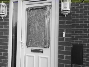 A front door with a hole, boarded up with plywood.