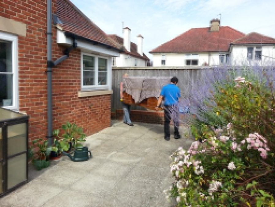 Removals men carry our sideboard out from the back door of New Earth.