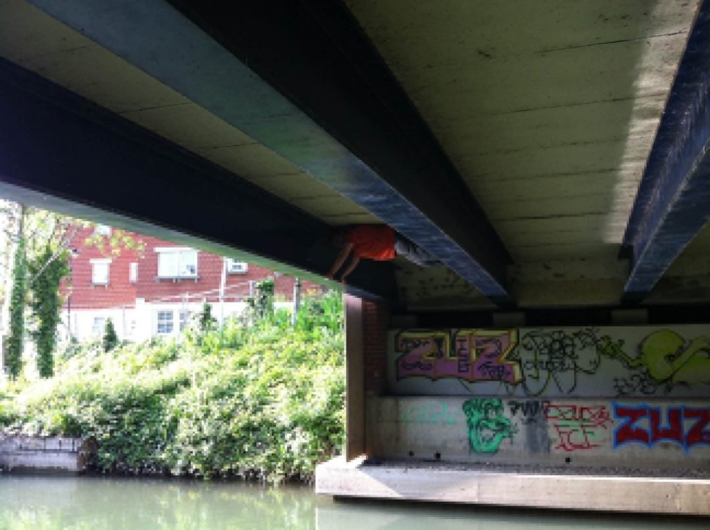 Dan, braced between two I-beams about 5 feet apart, underneath a bridge.