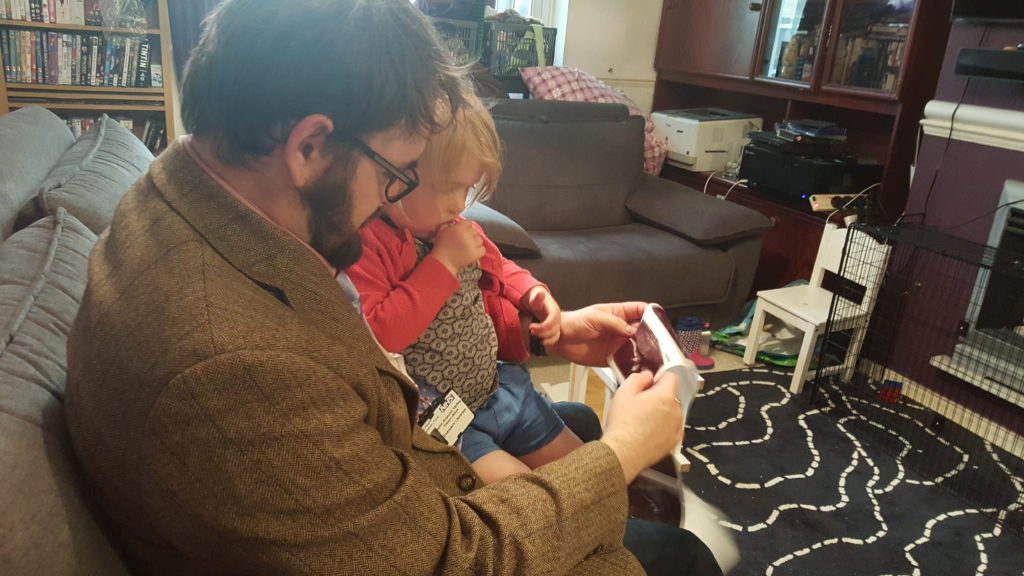 Annabel sitting on her daddy's knee and looking at sonograph pictures of her future baby brother.