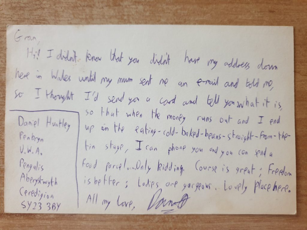 Postcard reading: Gran, Hi! I didn't know that you didn't have my address down here in Wales until my mum sent me an e-mail and told me, so I thought I'd send you a card and tell you what it is, so that when the money runs out and I end up in the eating-cold-baked-beans-straight-from-the-tin stage, I can phone you and you can send a food parcel... Only kidding. Course is great; freedom is better; ladies are gorgeous. Lovely place here. All my love, Dan