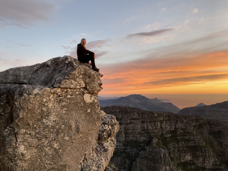 Dan sitting on a rock on Table Mountain, Cape Town, with a sunset in the background