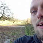 Dan walking through a field, enormous muddy patch behind