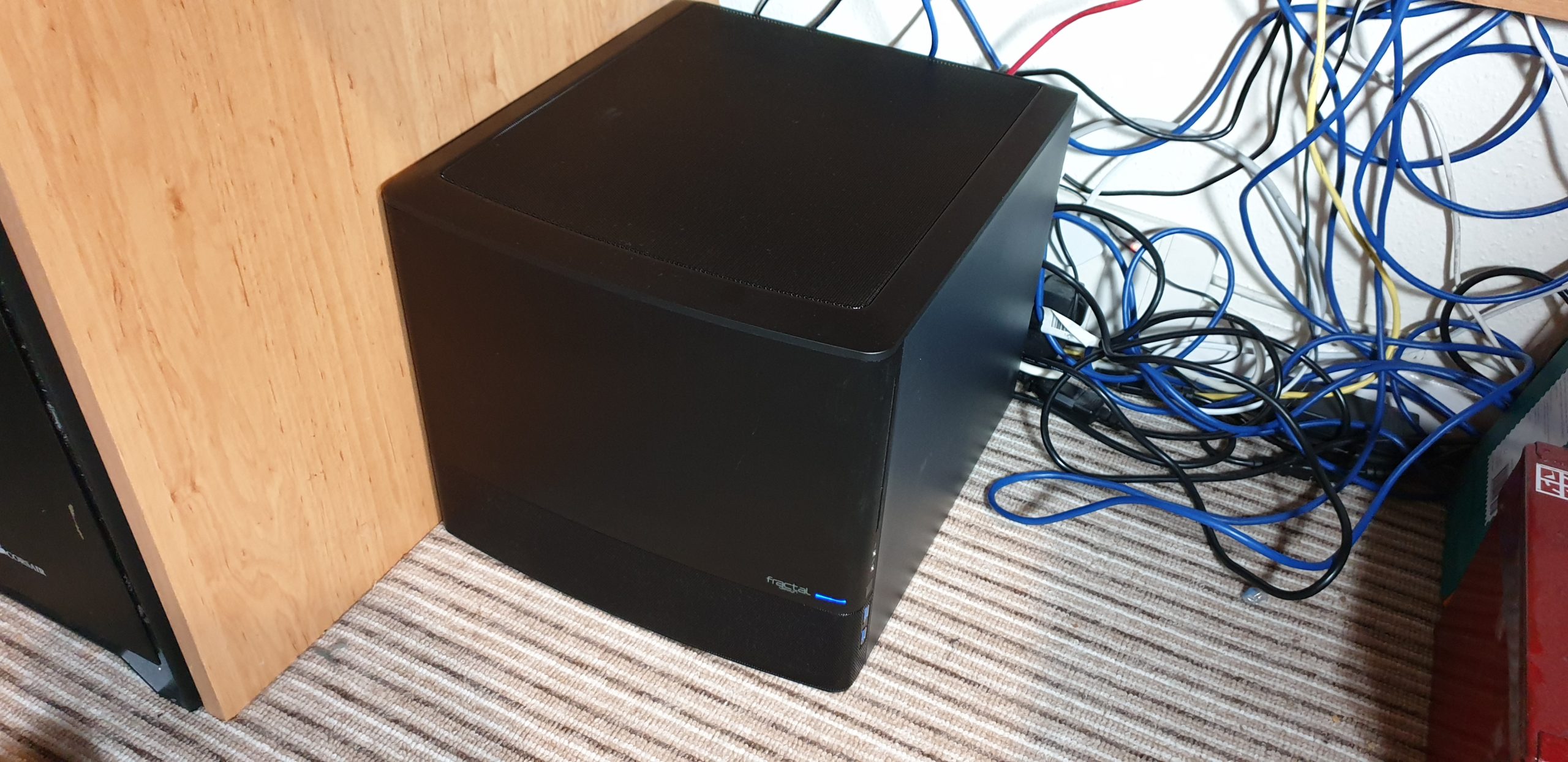 A black computer "cube" nestled under a desk, amongst cables.
