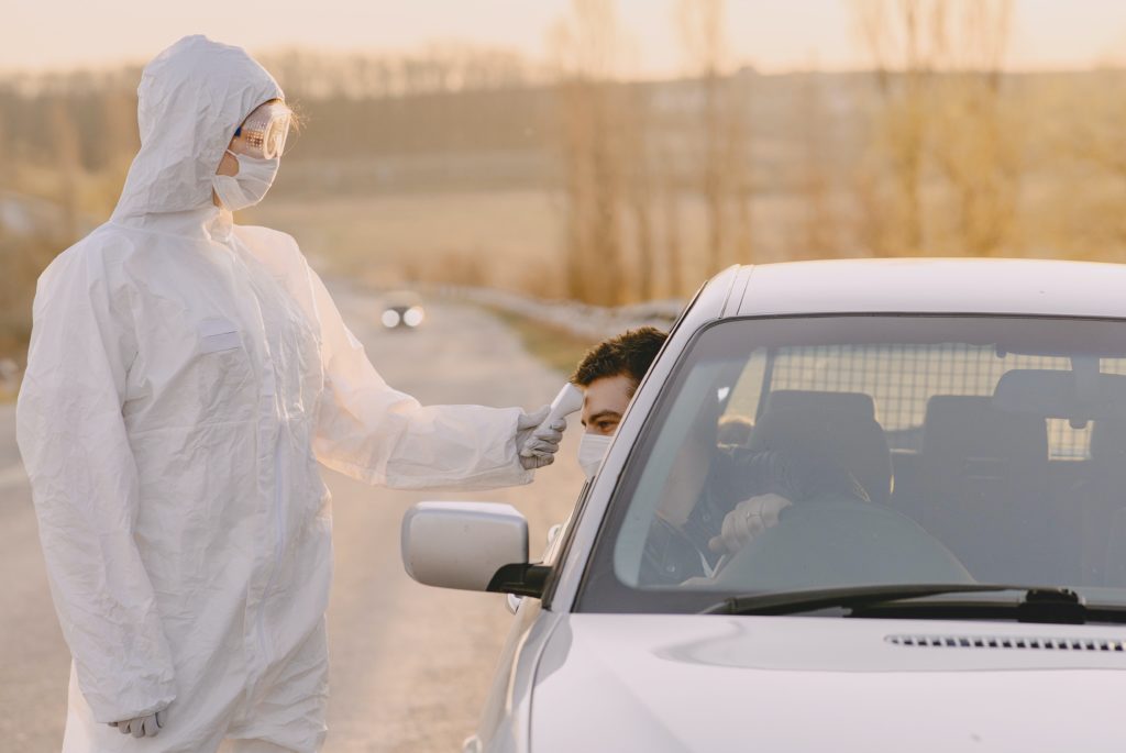 Driver's temperature being checked at the roadside by somebody in full protective equipment.