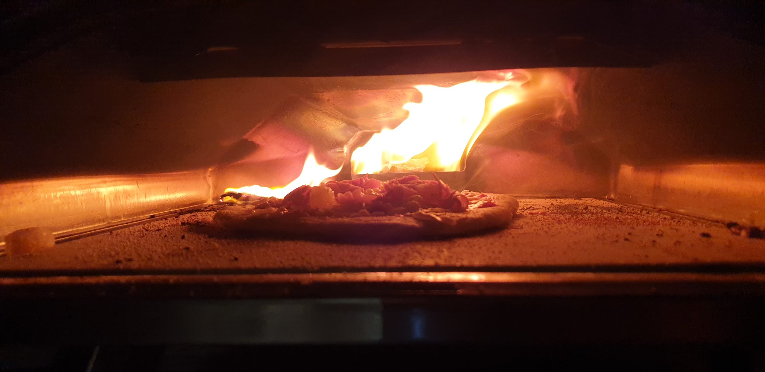 Pizza in an oven, fire raging behind and jumping onto the floor of the oven.