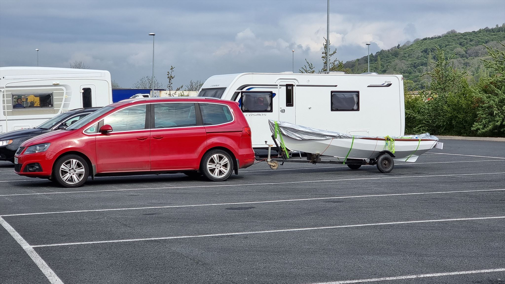 Arthur (red car) and Lucy (rowboat in tow) parked at a service station alongside caravans and HGVs