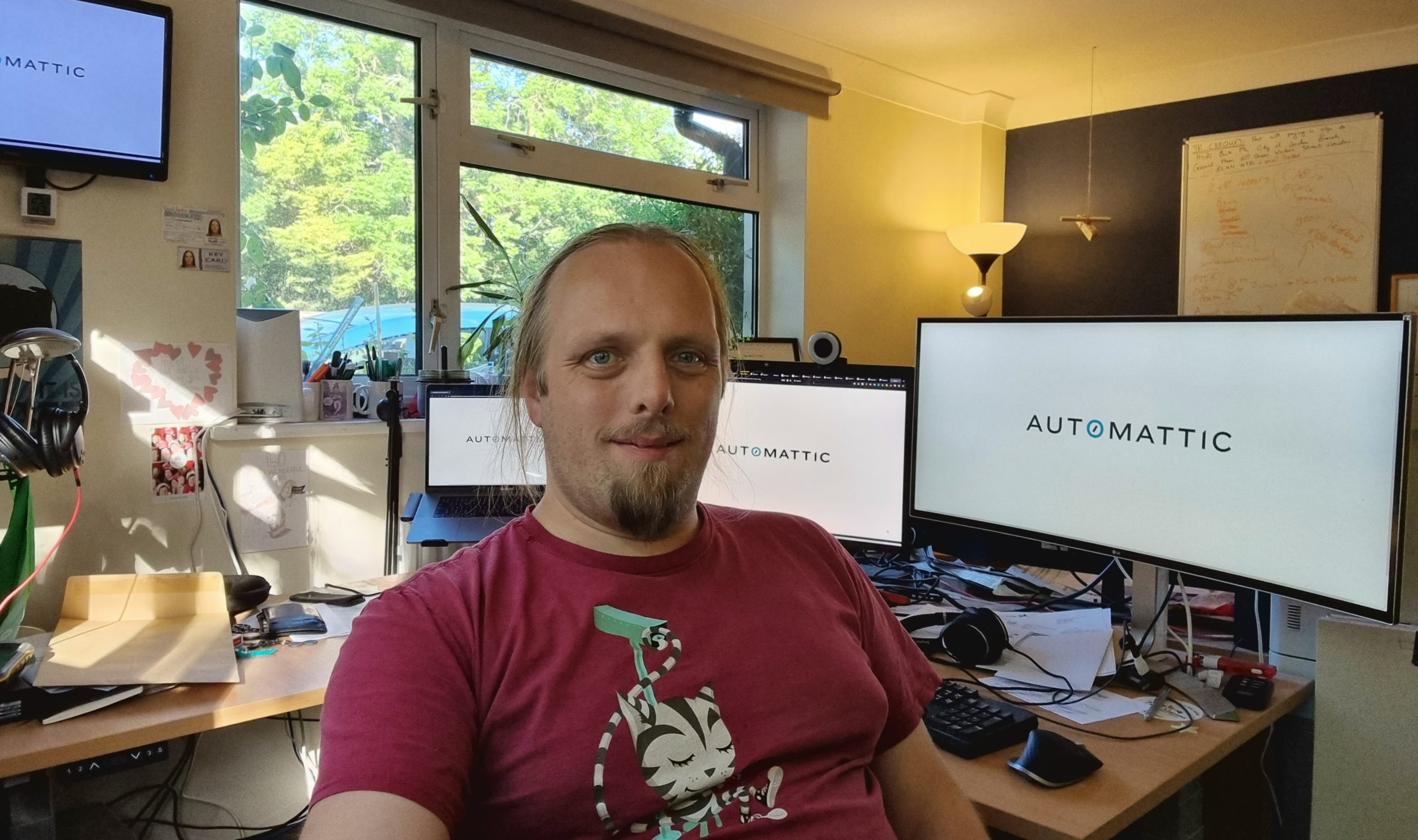 Dan sits in his office; behind him, four separate monitors show the Automattic logo.