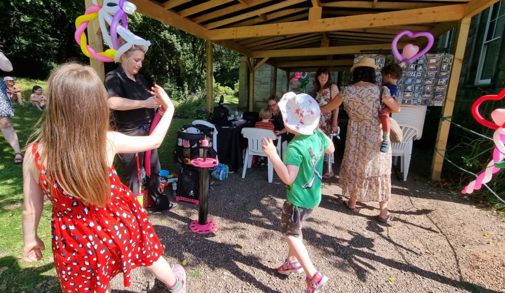 A balloon artist wearing a unicorn on her head makes sculptures for children.