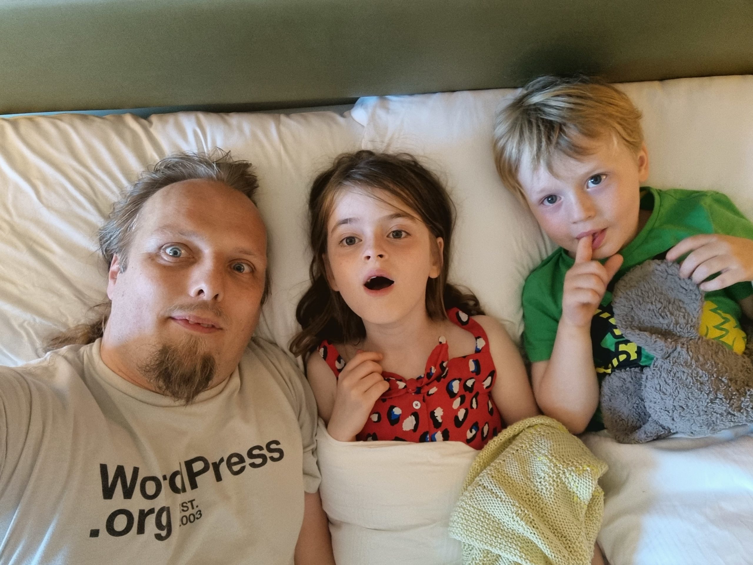 Dan and the kids in a bed at a hotel.