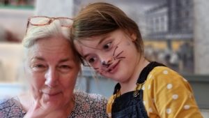 A woman and a girl; the girl is face-painted as a cat, the woman has bit of the face paint rubbed off onto her.