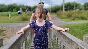 A girl shouts with excitement as she crosses a wobbly bridge.