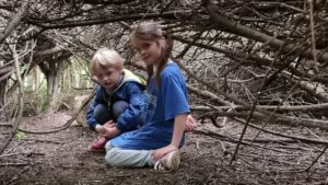 Two children crawl through a den of sticks.