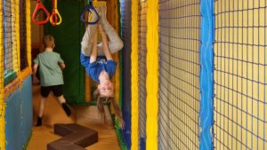 A girl hangs upside-down in a soft play area.