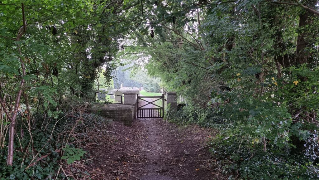 Churchyard gate at the end of a tree-lined path.