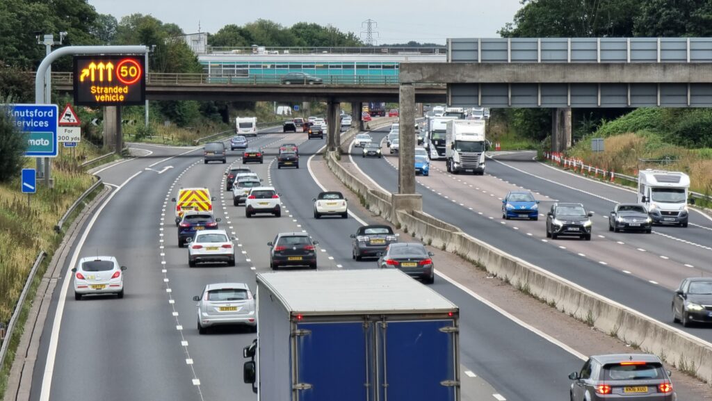 Motorway traffic moving past a 50 limit and "stranded vehicle" warning sign.