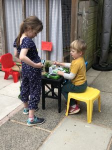 Children play shop: a boy operates a checkout and a girl buys shopping.