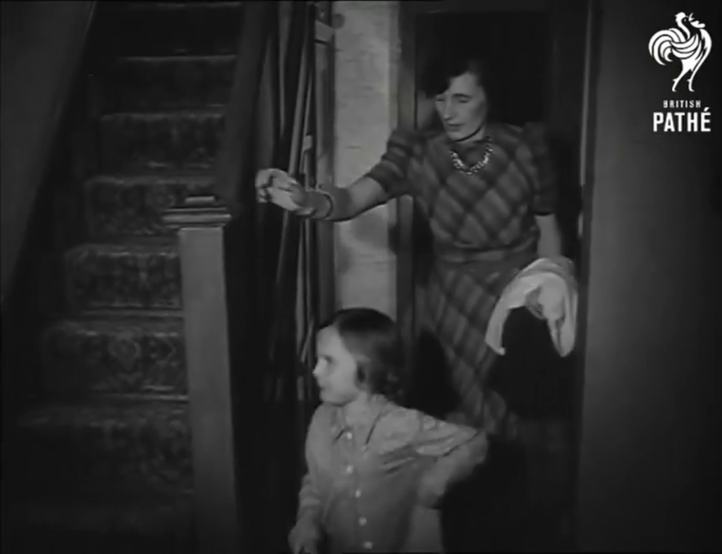 Black & white framegrab showing a woman following her child, wearing pyjamas, towards a staircase up.