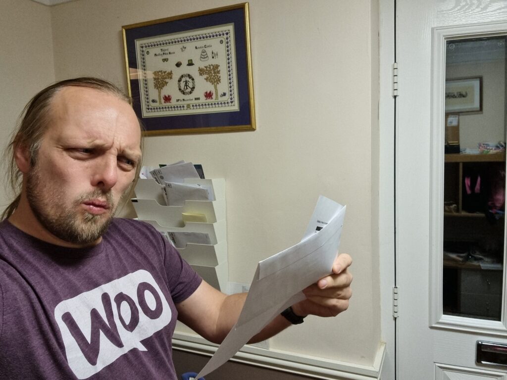 Dan, near his front door, reads his mail. His facial expression suggests that he's about to exclaim "What!?"