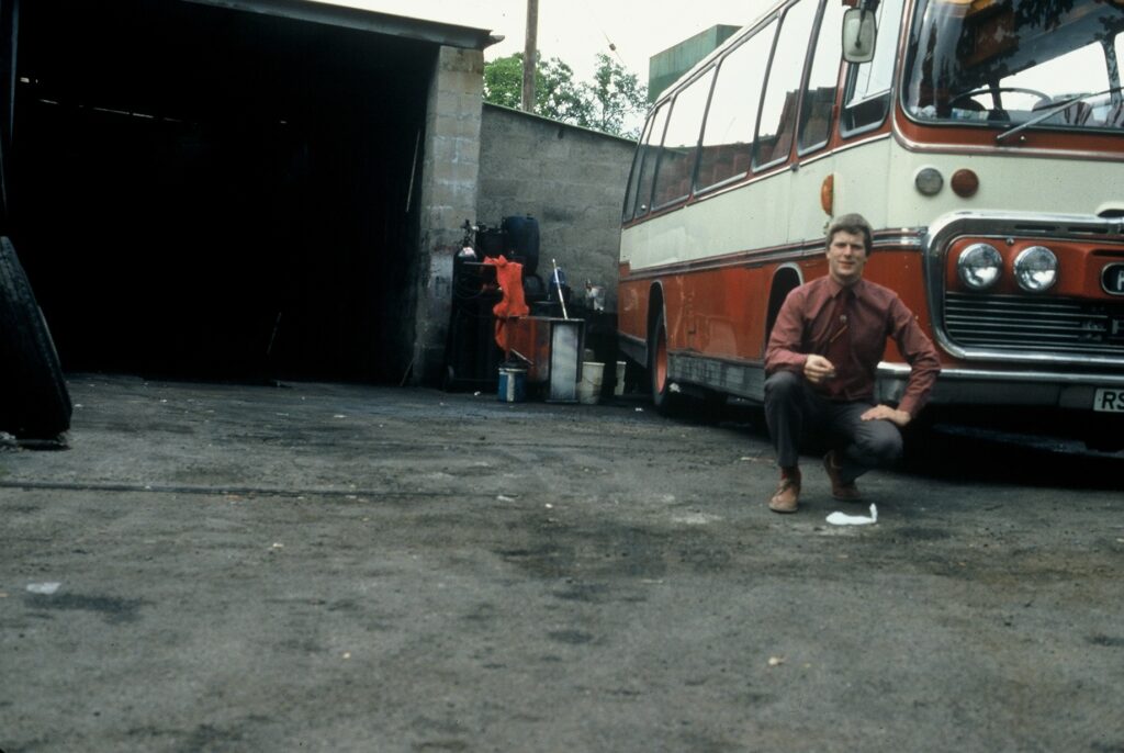 Dan's dad crouches next to a bus in a somewhat lopsided-photo.