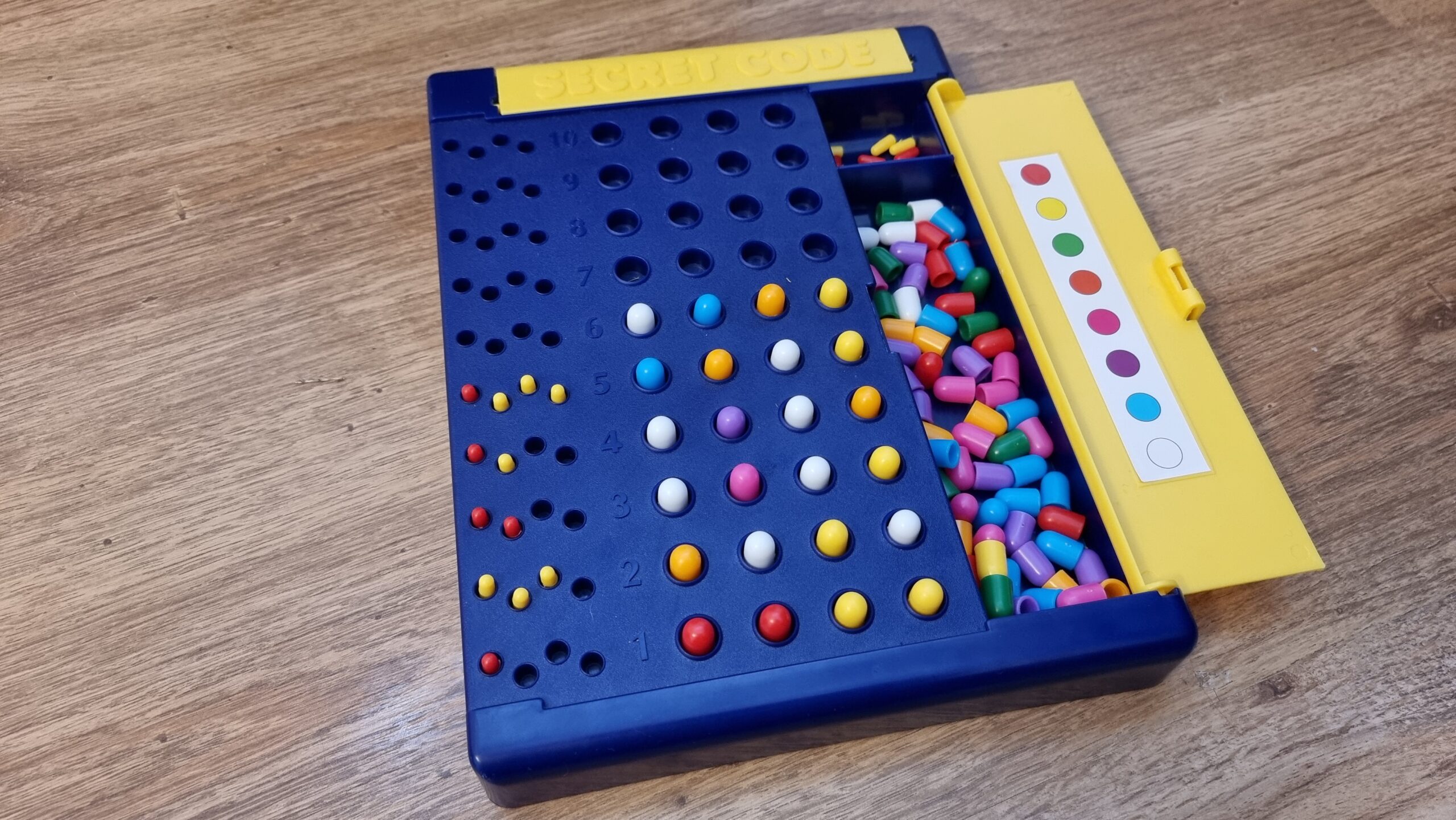 A plastic Mastermind board in blue and yellow with ten guess spaces and eight pegs. The sixth guess is unscored but looks likely to be the valid solution.