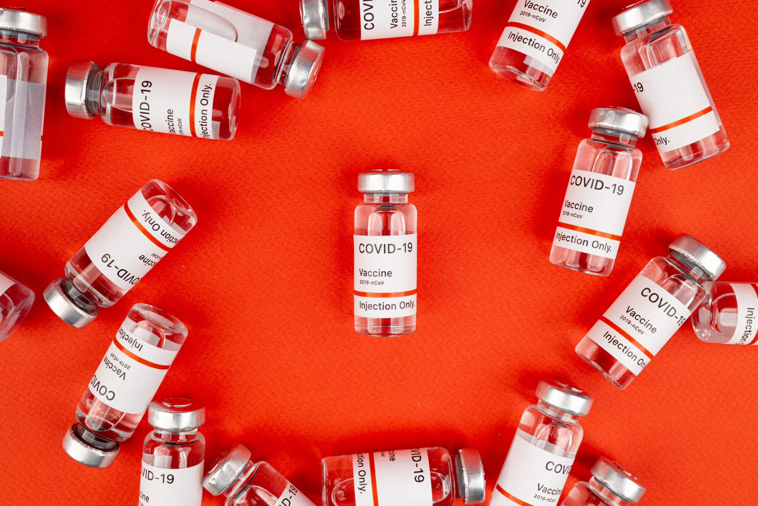 Vials of Covid vaccine scattered across a red background. Photo courtesy Maksim Goncharenok.
