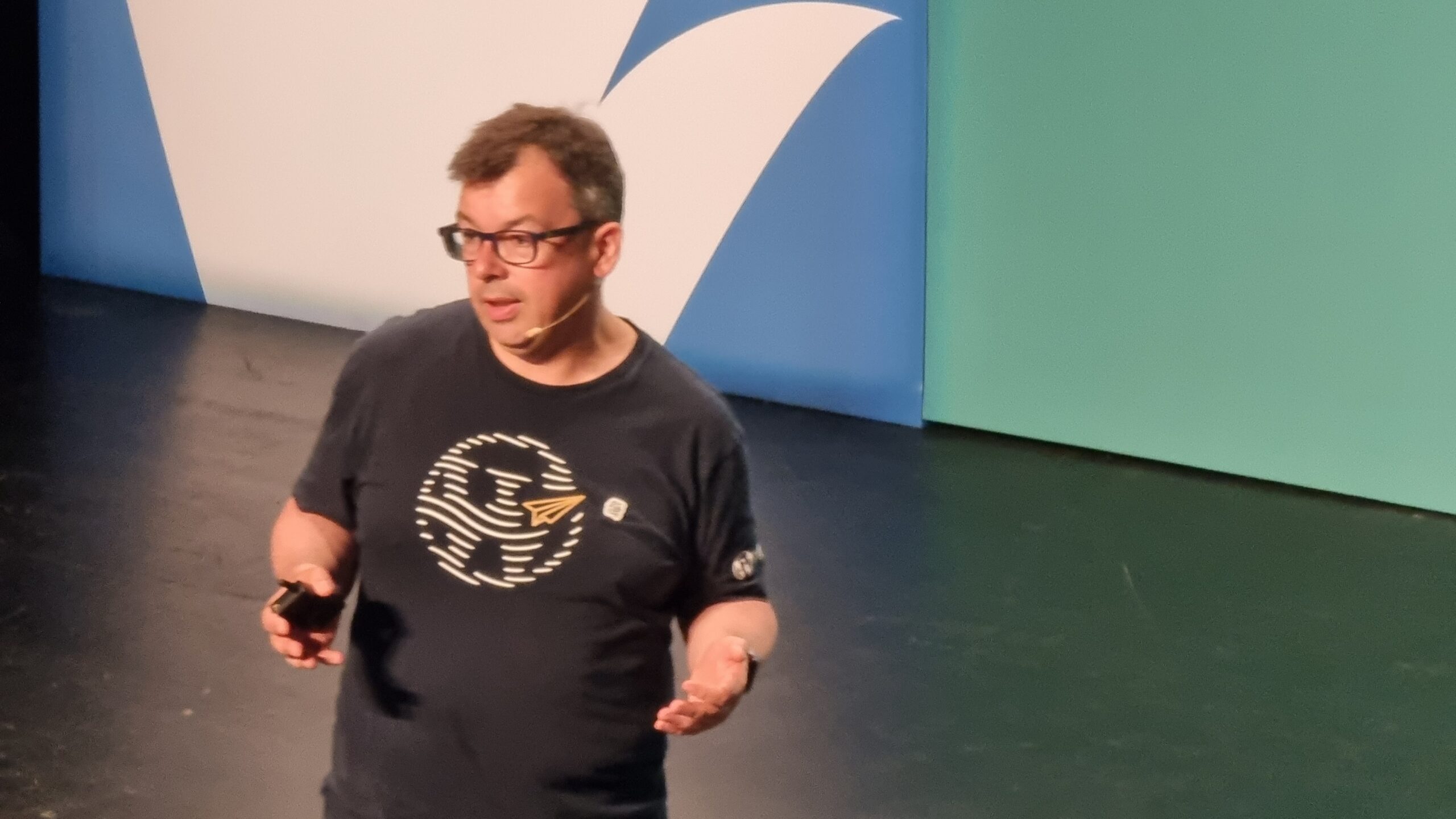 A man wearing glasses and a t-shirt with a WordPress logo stands on a stage.