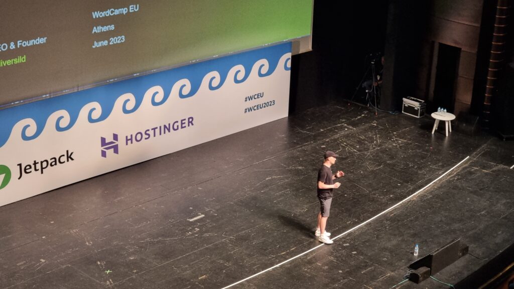 A man in a literal black hat stands in the centre of a large theatre stage.