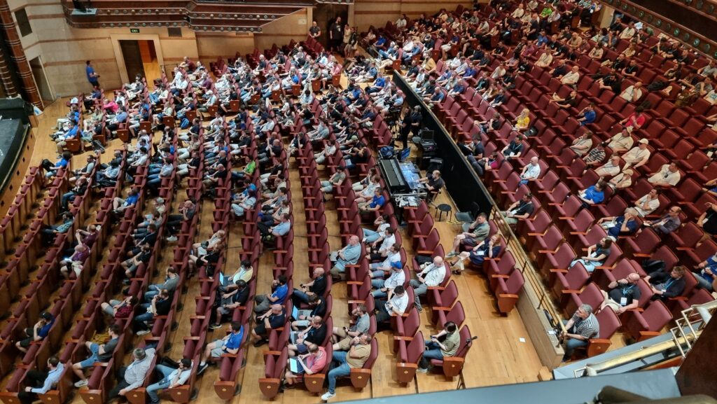 A large audience of a few hundred people, seen from above, facing left.