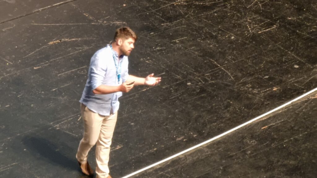 A man in a blue shirt stands on a large stage.