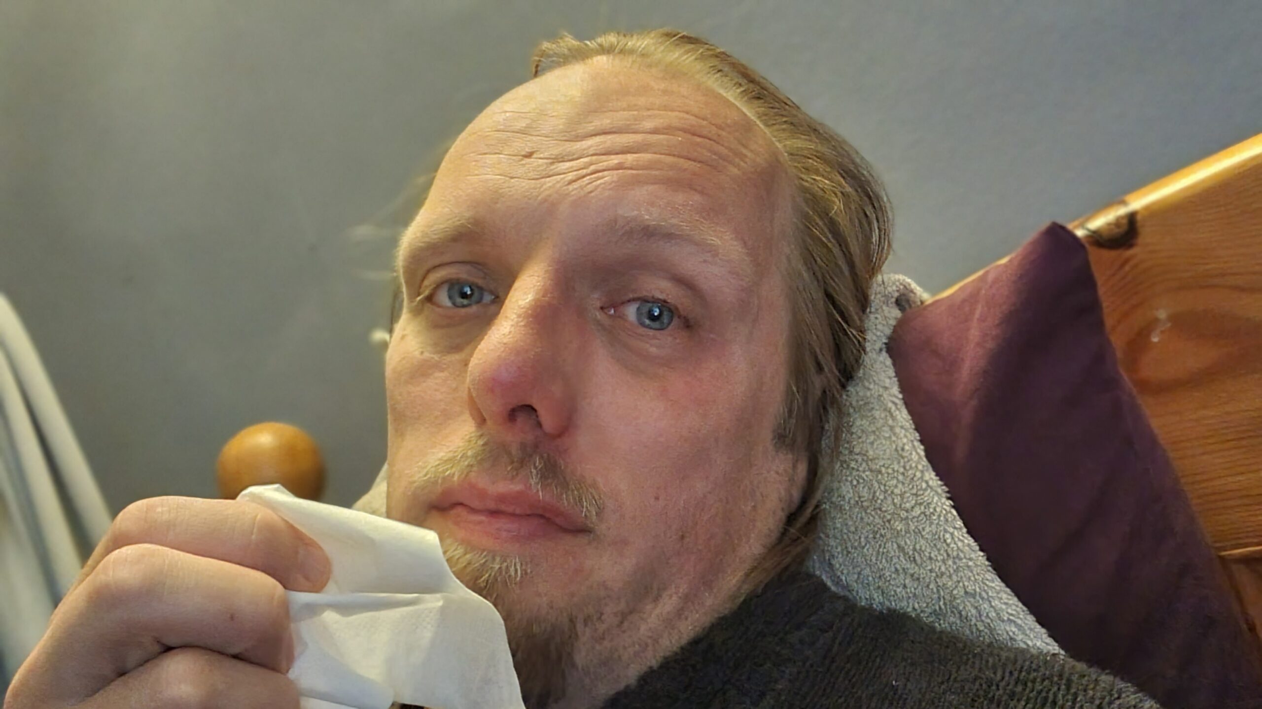 Dan, sitting in bed, holding a tissue and looking unwell.