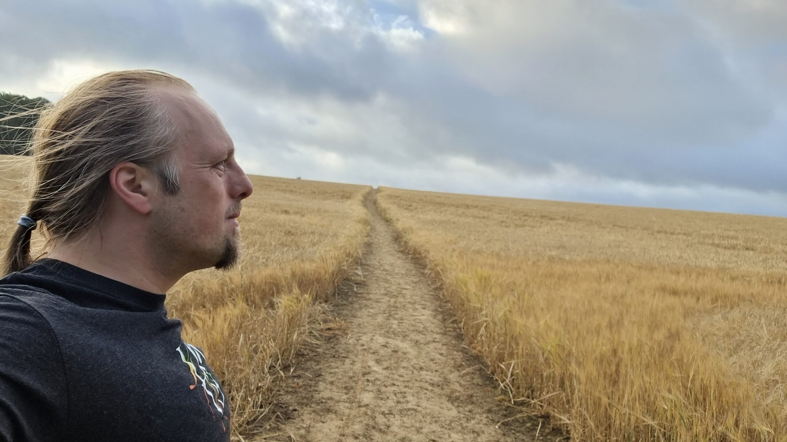 Dan, on a path through a young cornfield, stares towards the distant clouds.