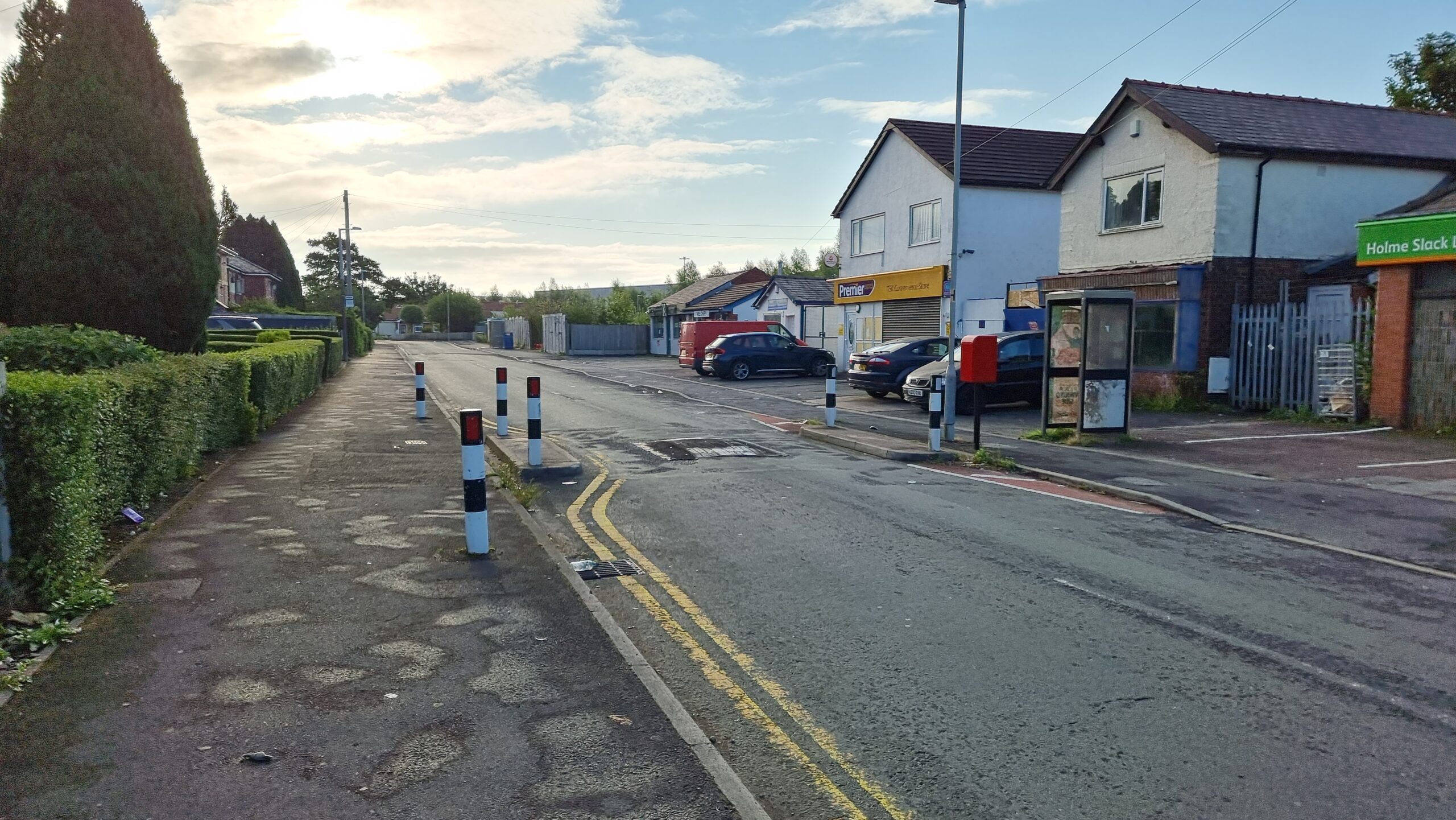 Photograph showing a suburban street in a Northern town, shortly after sunrise. The belittered street is worn and the decrepit husk of a telephone box stands outside an abandoned store front.