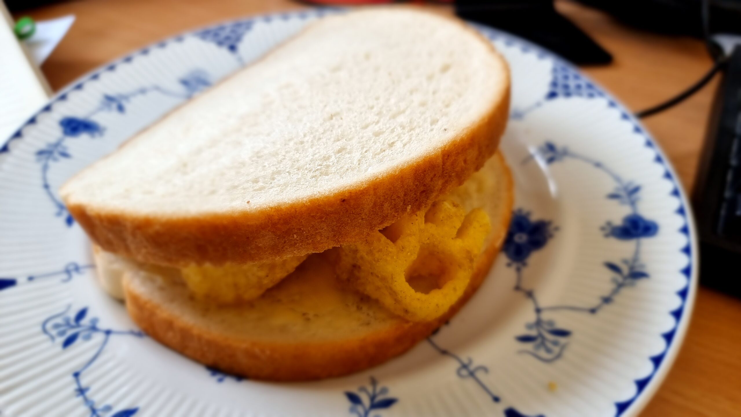 Thich white sandwich on a blue-and-white china plate, with the distinctive shape of an organge-coloured Monster Munch crisp poking out.