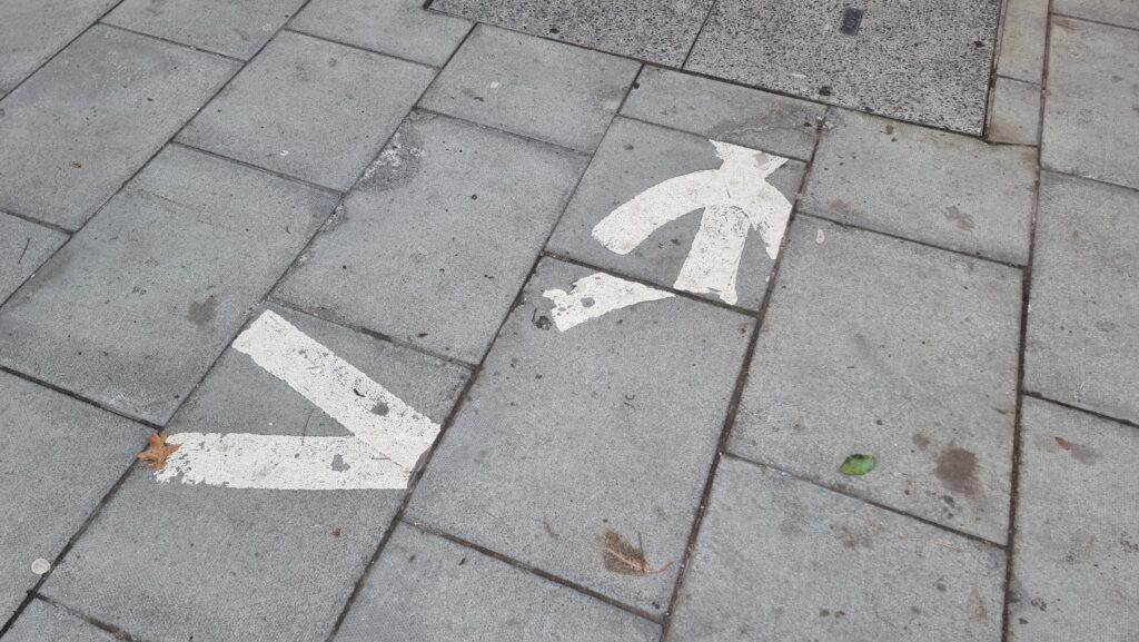 Photograph of paving slabs: a glyph of a walking person, signifying "walk here", has been painted onto the flagstones, but the stones have since been lifted and replaced in slightly different locations, making the person appear "scrambled".