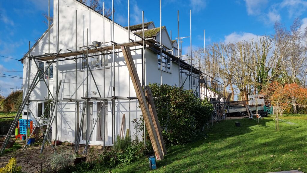 Photograph showing a detached white house clad in scaffolding, under a clear blue sky.