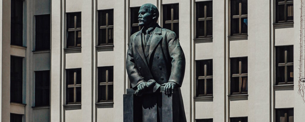 Photograph of the Statue of Lenin in Independence Square, Minsk: Government House #1 stands behind a large metal statue of Vladimir Lenin, looking to his right.