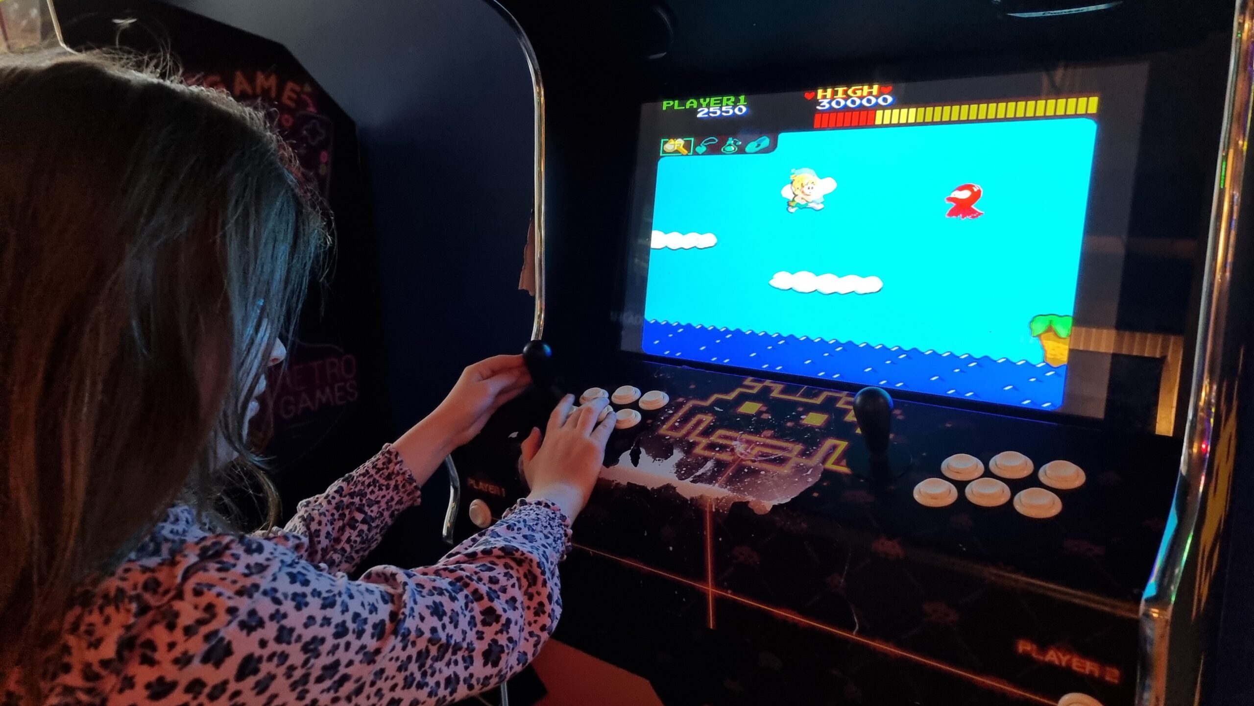 A young girl in a pink leopard-print top plays Wonder Boy on an arcade cabinet.