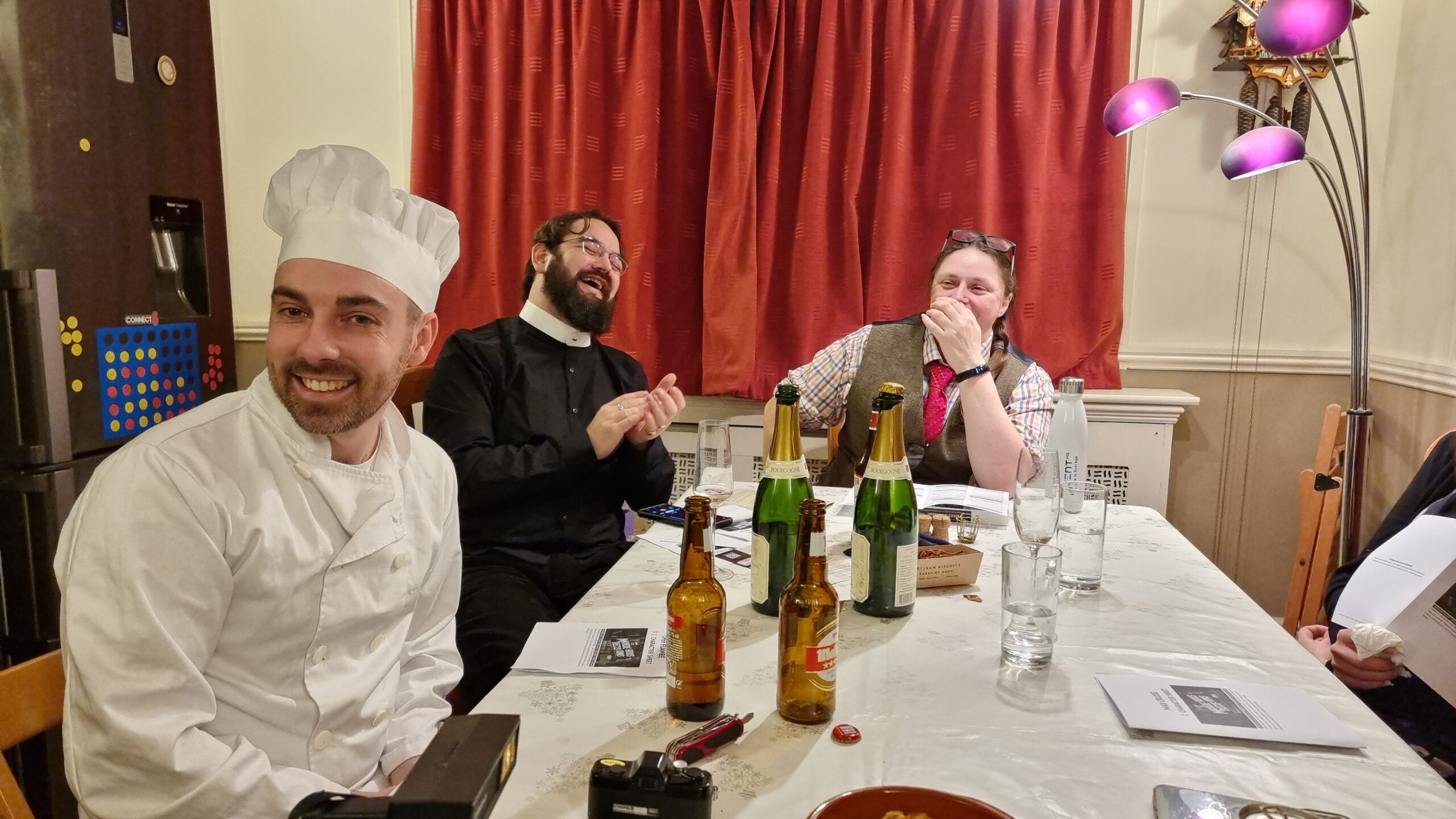Guests dressed as a chef, a priest, and a librarian sit around a dining table at a murder mystery party.