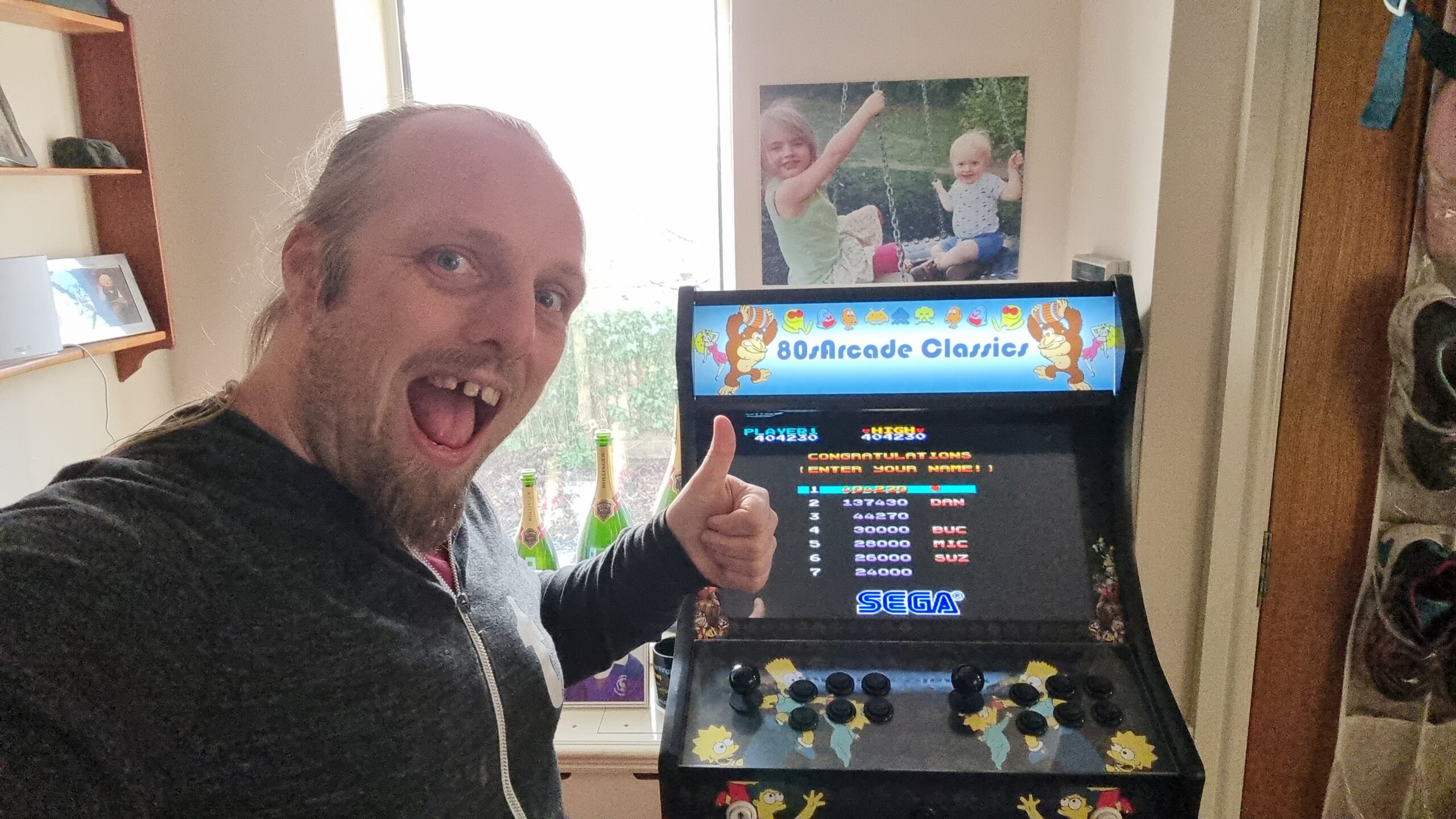 Dan with his thumbs-up in front of the high-score table (with the top-ranking spot about to be filled) of Wonder Boy, on a generic "80s Arcade Classics" arcade cabinet.