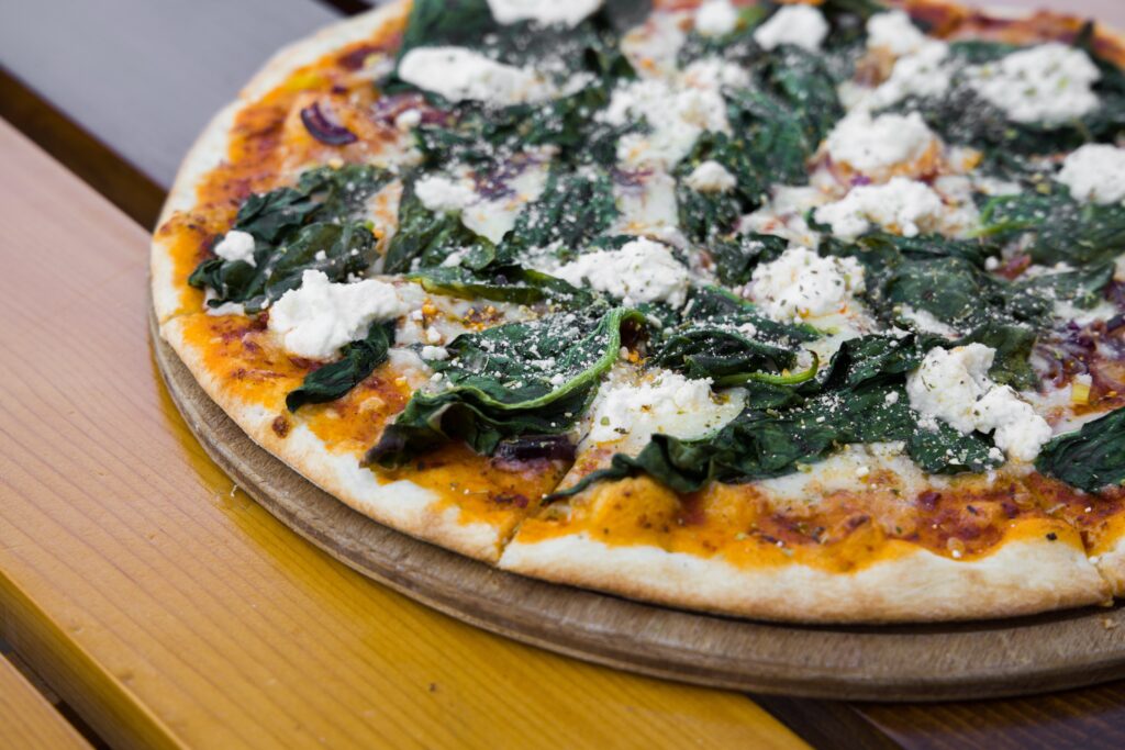 Freshly-baked pizza with spinach and mushrooms, whole, on a wooden board.