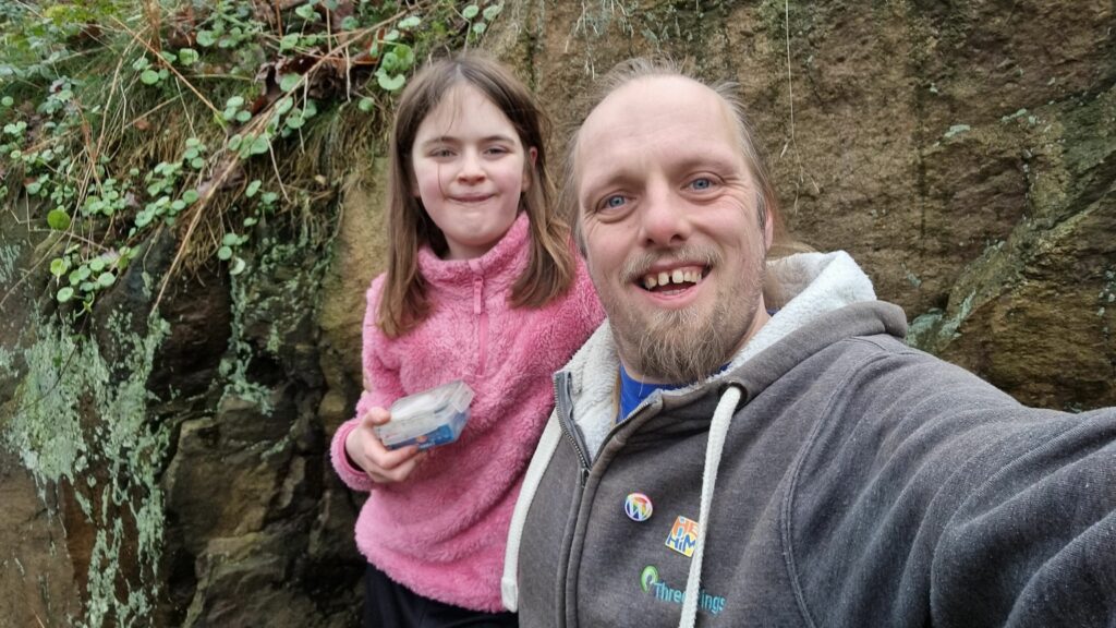 Dan smiles alongside a 10-year-old girl who's holding a geocache container.