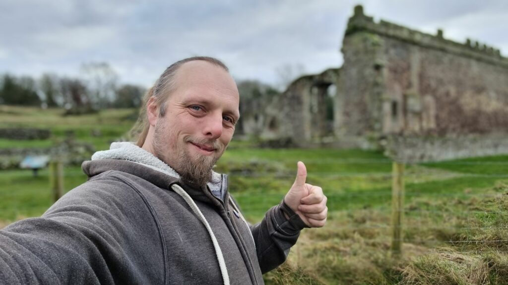 Dan, with his thumb up, in front of the ruin of an abbey.