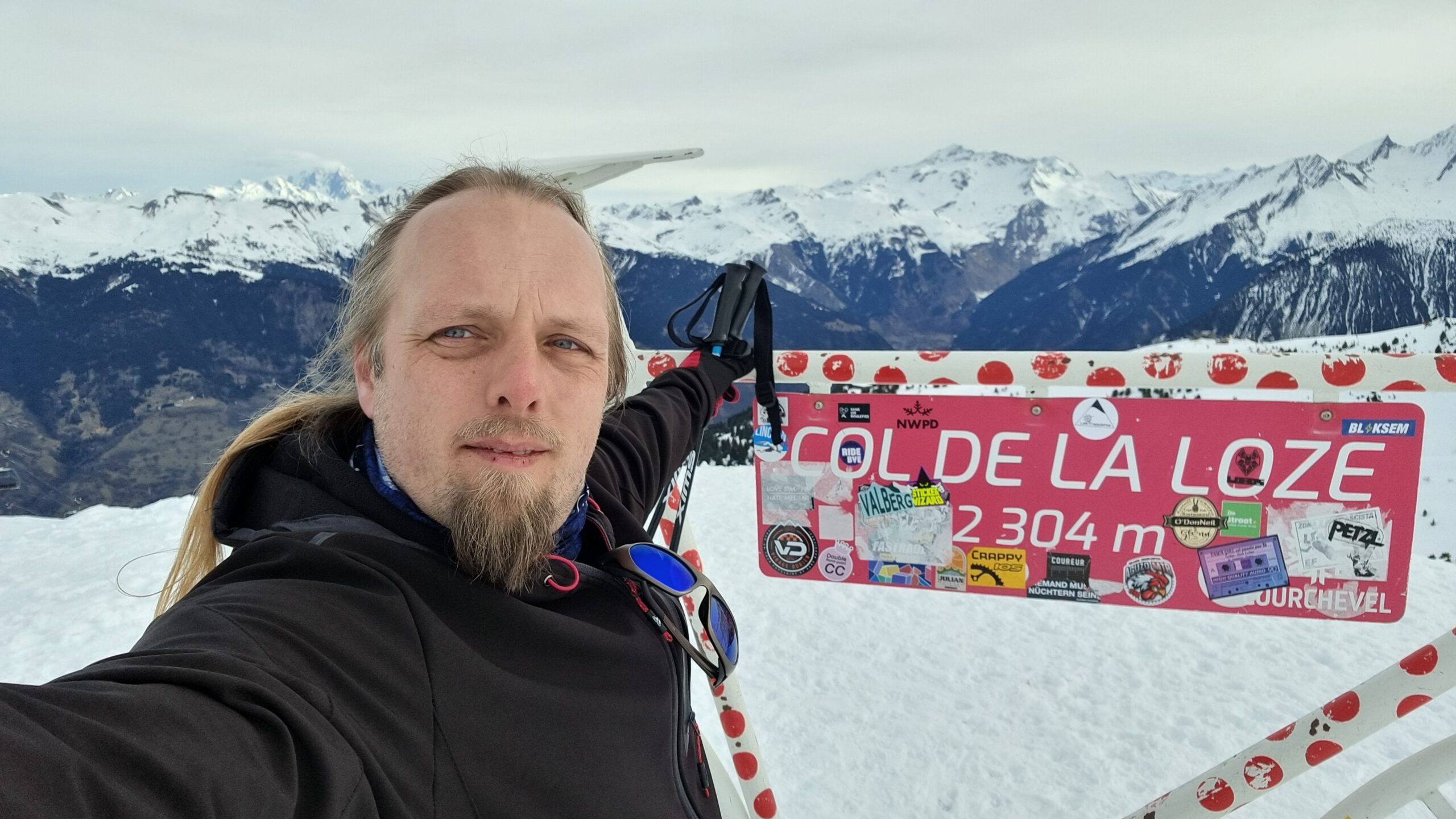 Dan, in a wintery mountainous landscape, poses for a selfie by a sculpture of a bicycle marking part of the route of the Tour de France. 