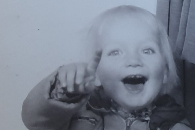 Monochrome photo of a toddler, smiling broadly, pointing at the camera.