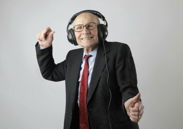 Cheerful white elderly man listening to music through headphones that are clearly too large for him.
