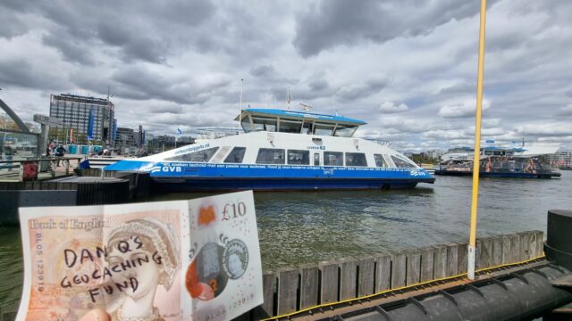 A £10 note with "Dan Q's Geocaching Fund" written on it in front of a ferry.