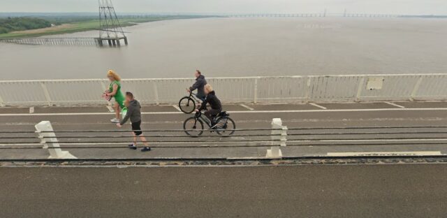 Cyclists alongside a 'motorway' river bridge lane.