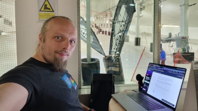 Dan sits at his laptop in a cafe; ski lifts can be seen in the background.