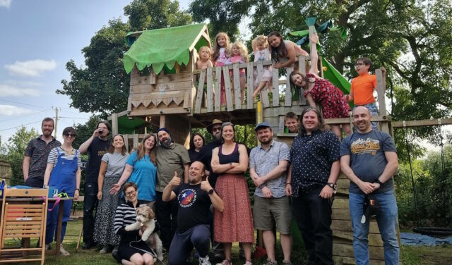 14 adults, 8 children, and a dog stand on/in front of a garden climbing frame: Dan is in the centre.